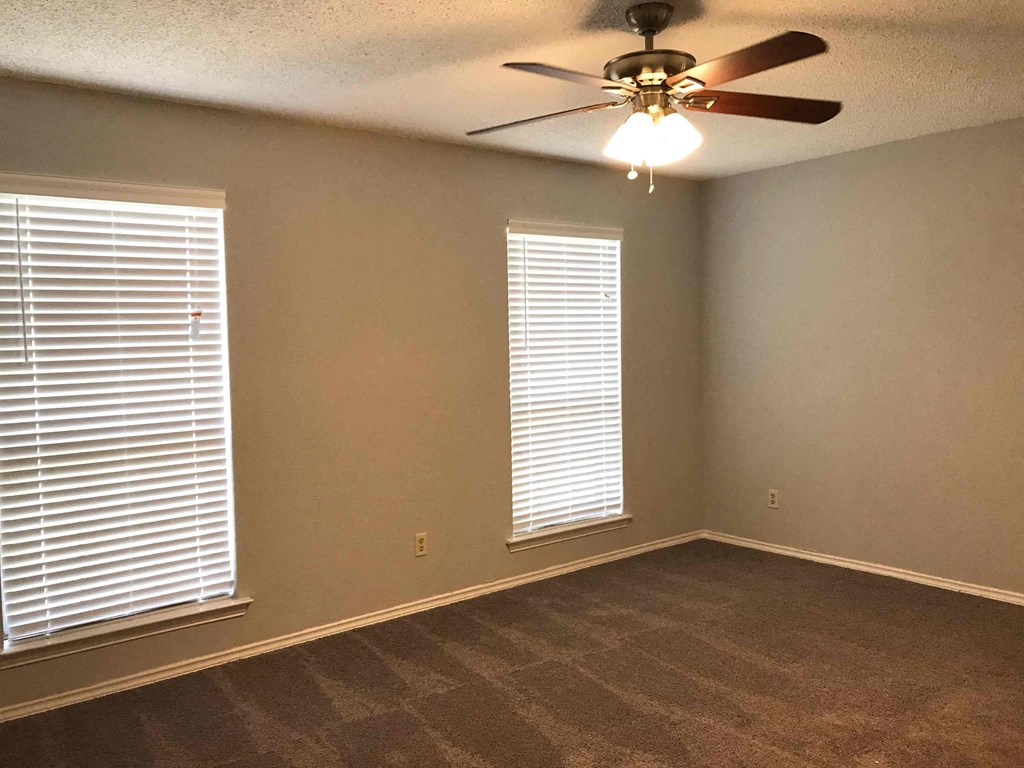 an empty living room with a ceiling fan and two windows