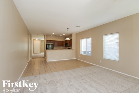 an empty living room with a kitchen in the background