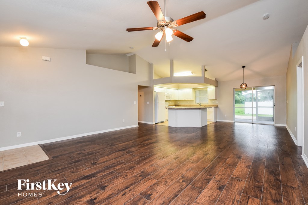 an empty living room with a ceiling fan and a kitchen