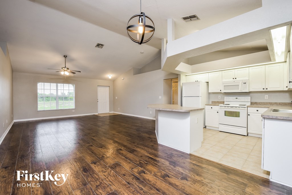an open kitchen and living room with white appliances and wood flooring