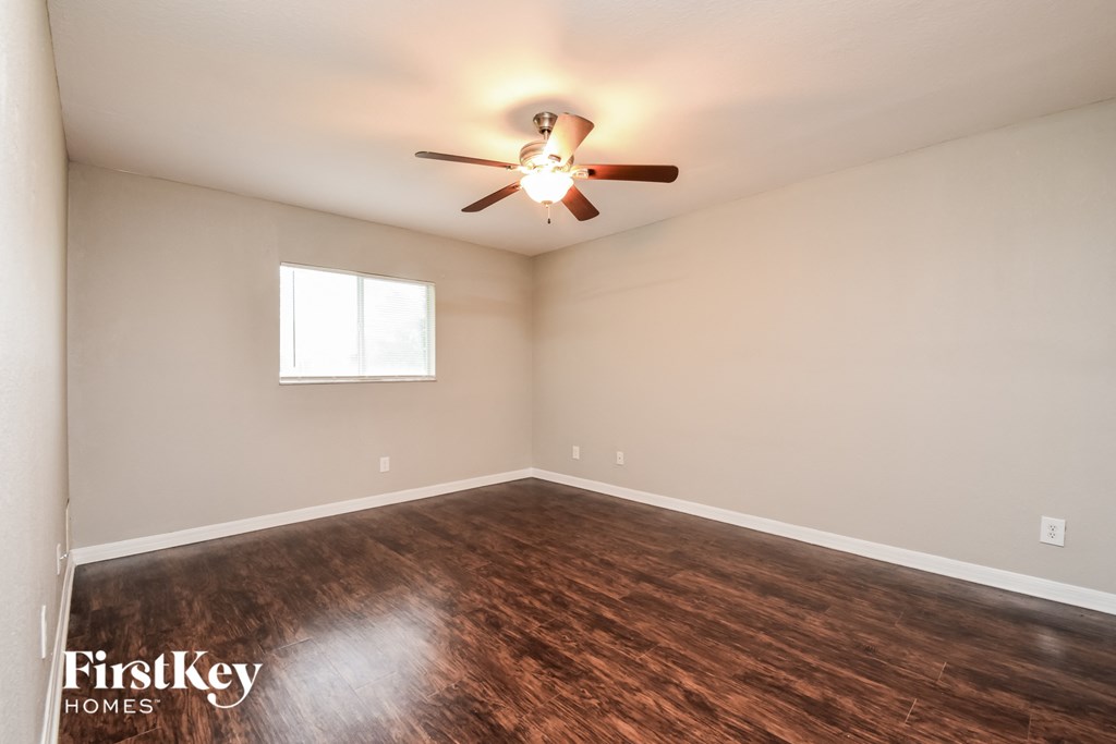 the spacious living room with hardwood flooring and a ceiling fan