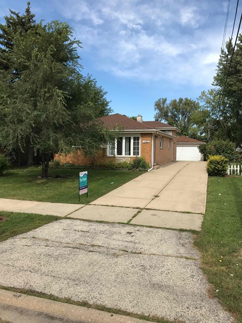 A house with a driveway and a sign on the lawn.