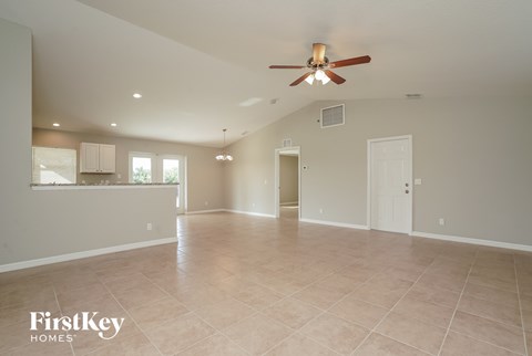 an empty living room with a ceiling fan and a kitchen