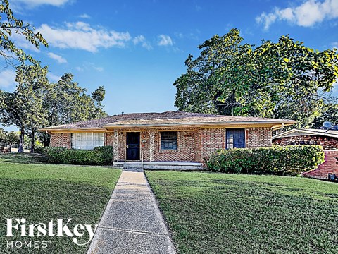 the front of a brick house with a lawn and a sidewalk