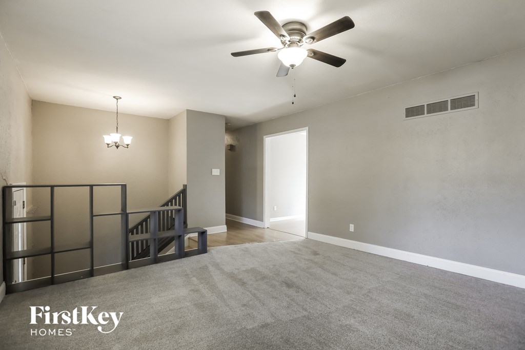 an empty living room with a ceiling fan and a staircase