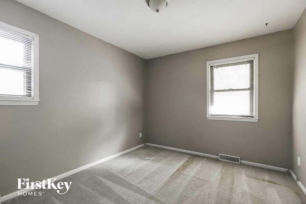 an empty bedroom with two windows and a carpeted floor