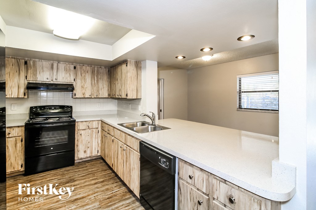 an updated kitchen with white countertops and wooden cabinets and black appliances