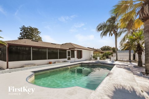 A pool in a backyard with a house and palm trees.