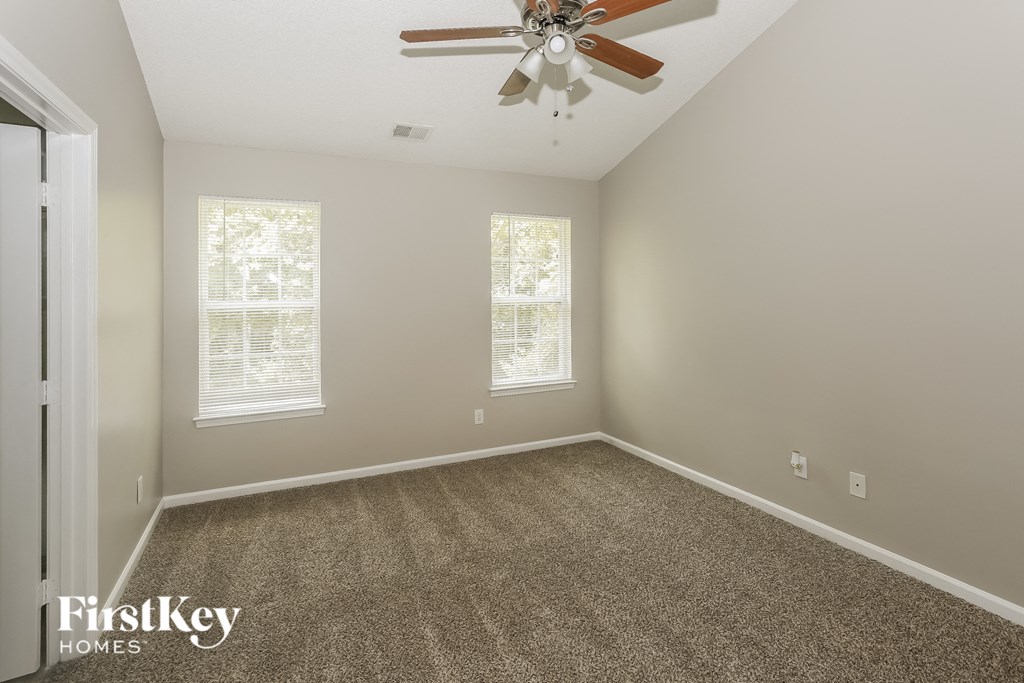 a carpeted room with a ceiling fan and two windows