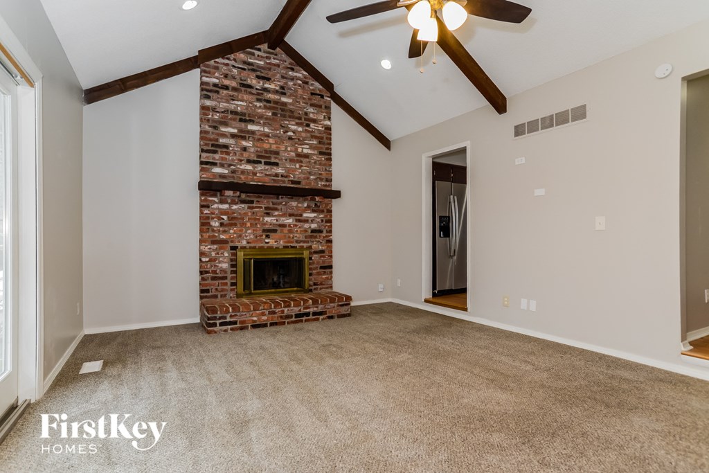 an empty living room with a brick fireplace and a ceiling fan