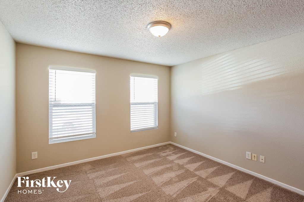 A room with a carpeted floor and two windows.