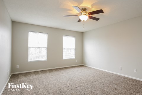 A spacious room with a ceiling fan and two windows.