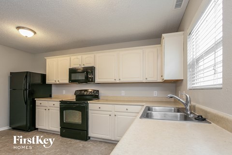 A kitchen with a black refrigerator, white cabinets, and a black stove top oven.