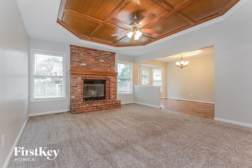 an empty living room with a brick fireplace and a ceiling fan