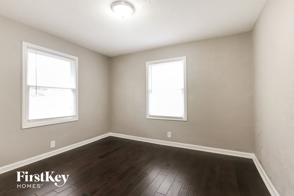 the interior of an empty room with wood flooring and two windows