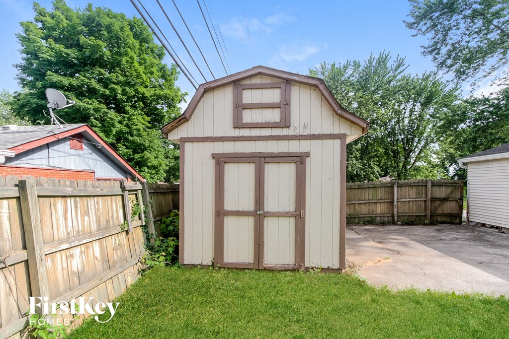 a small white shed with a door on the side of a fence