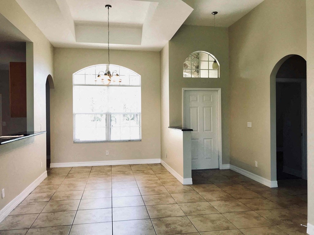 A large room with a white door and a window with a chandelier hanging from the ceiling.