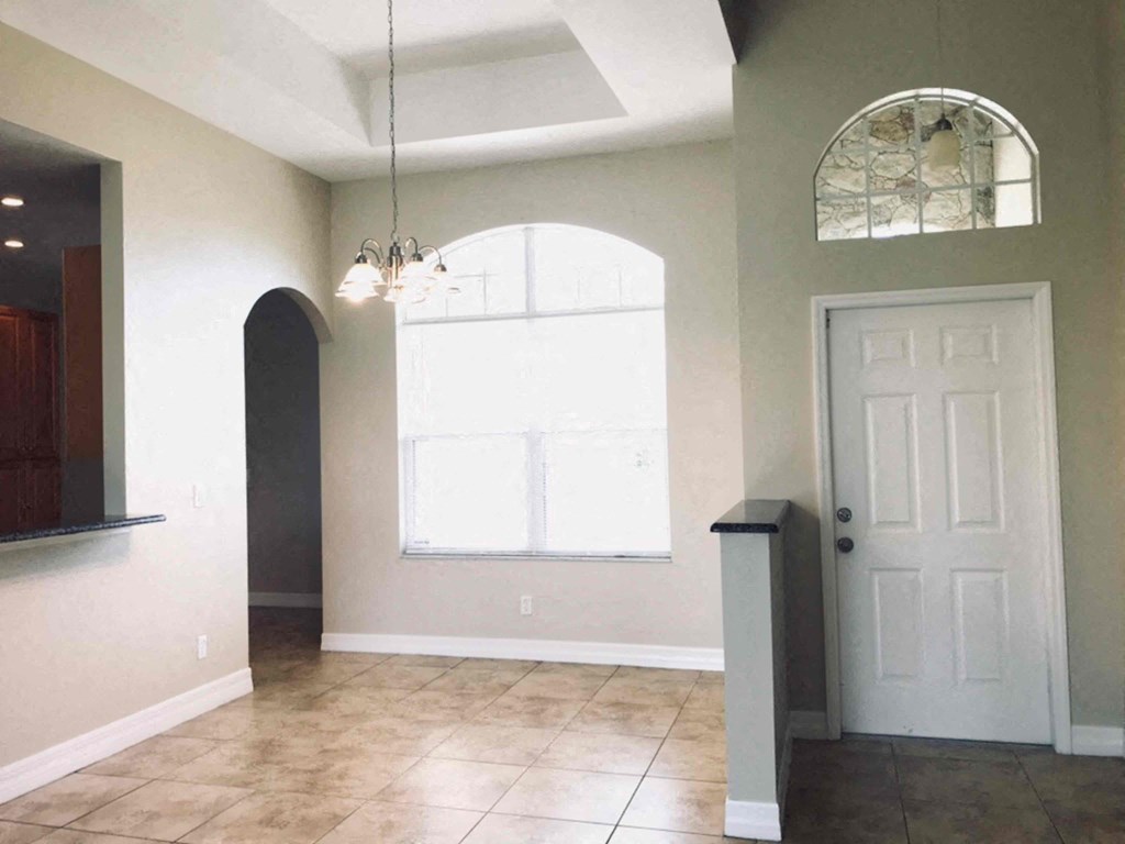 A room with a white door, a window, and a chandelier.