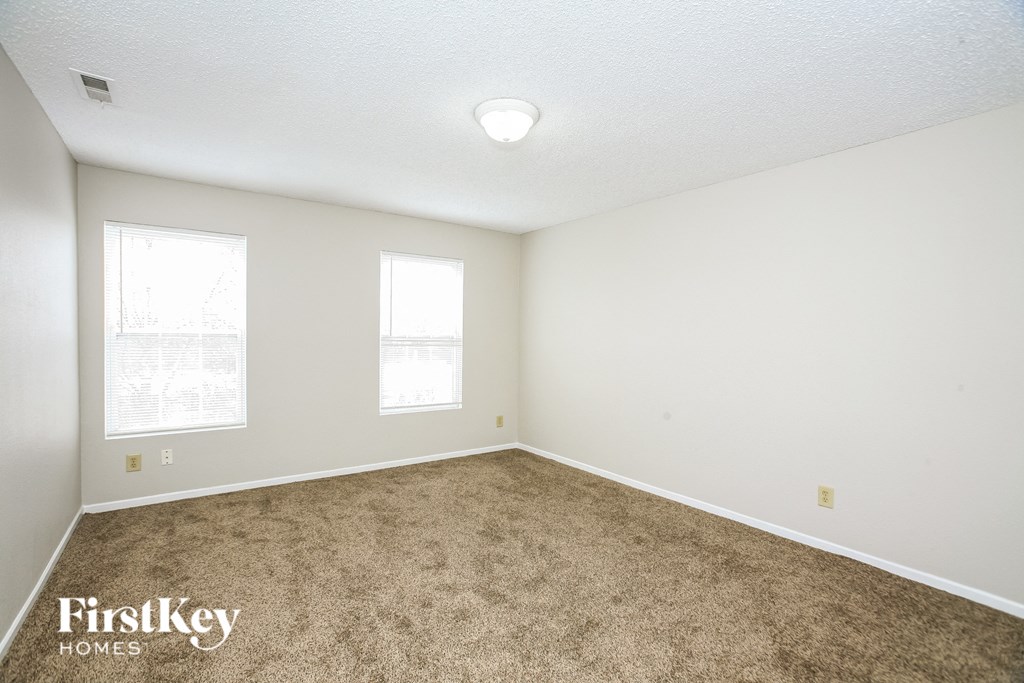 A room with a carpeted floor and two windows.