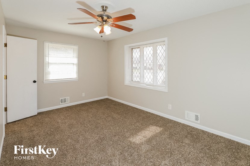 A room with a ceiling fan and two windows.