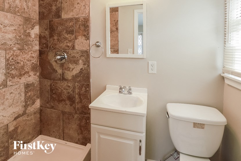 A bathroom with a brown tiled shower, a white sink, and a white toilet.