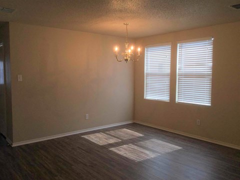 an empty living room with a chandelier and two windows