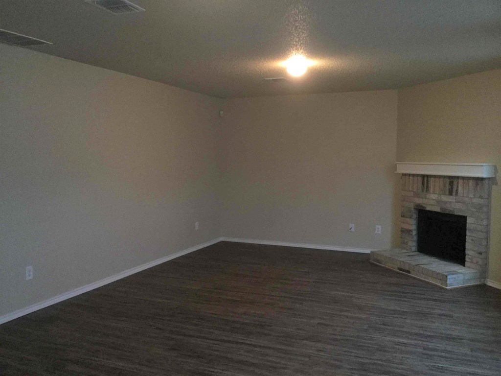 an empty living room with a fireplace and wooden floors