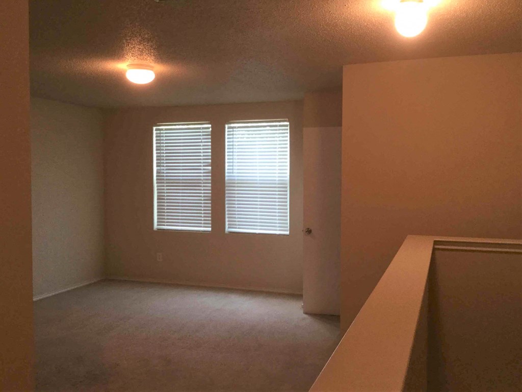 an empty living room with two windows and a bar