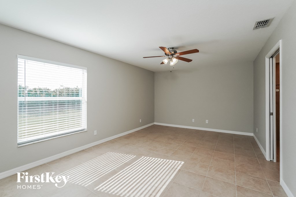 an empty living room with a large window and a ceiling fan