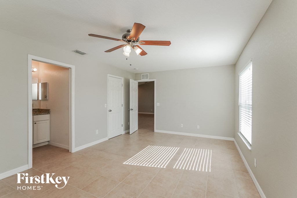 an empty living room with a ceiling fan and a door to a kitchen