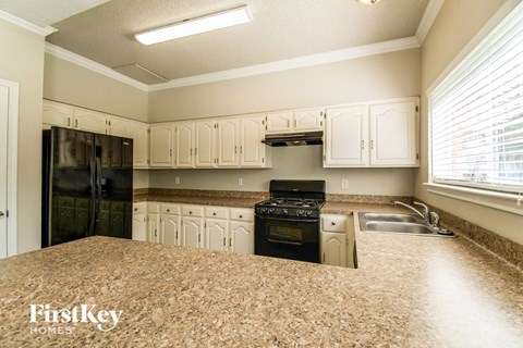 A kitchen with a black fridge, stove and white cabinets.