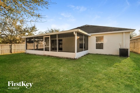 A house with a white exterior and a black roof is surrounded by a fence and has a grassy yard.