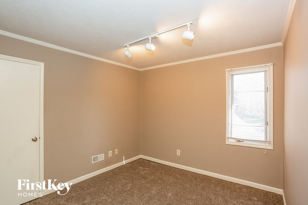 the bedroom of a house with brown carpet and a window