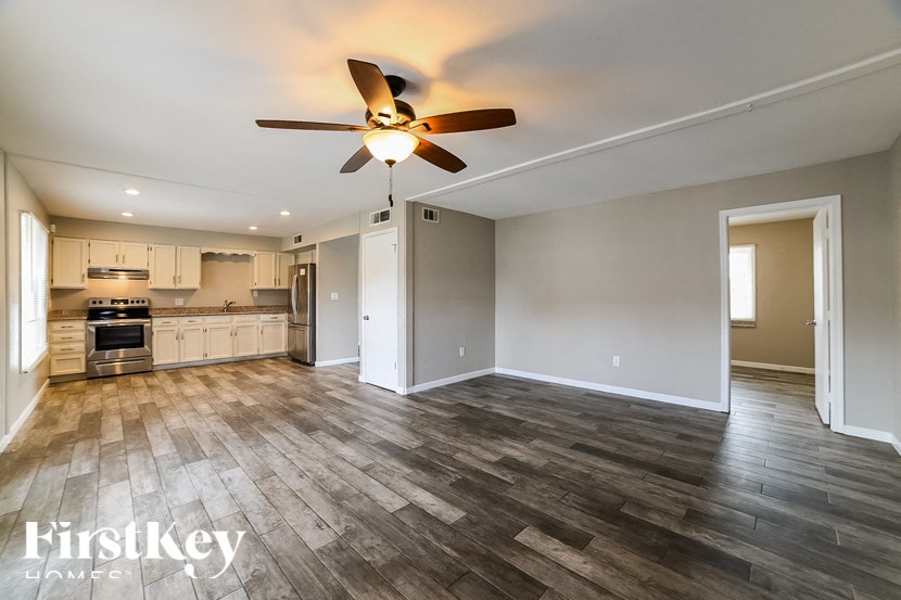 an empty living room with a ceiling fan and a kitchen