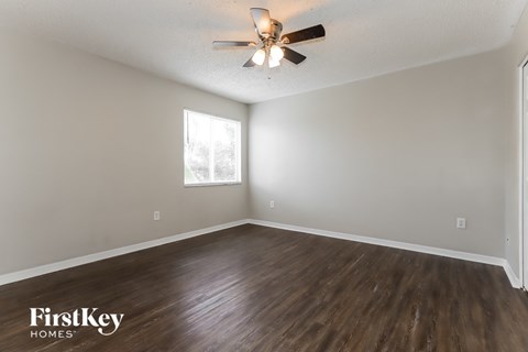the spacious living room with hardwood flooring and a ceiling fan