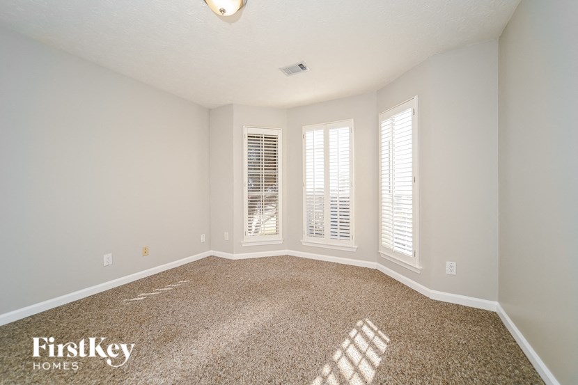 A room with a carpeted floor and two windows with blinds.