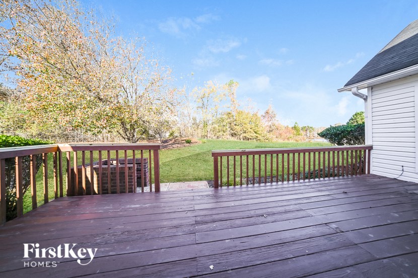 A wooden deck with a bench and trees in the background.