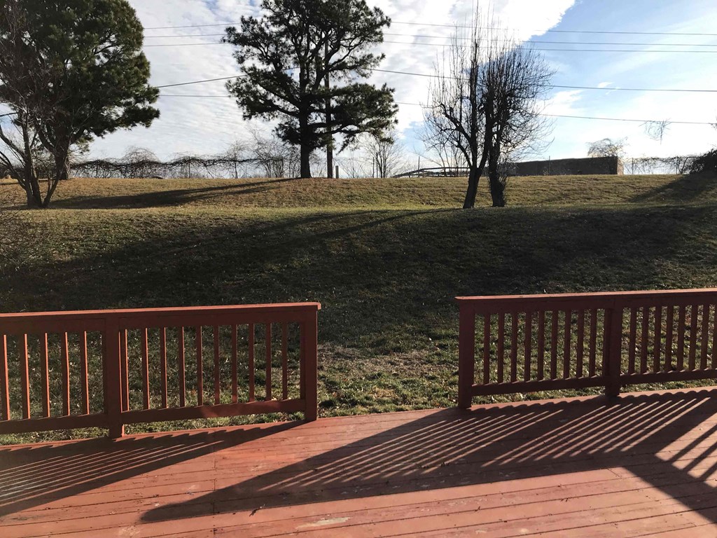 A wooden deck with a railing overlooks a grassy field.