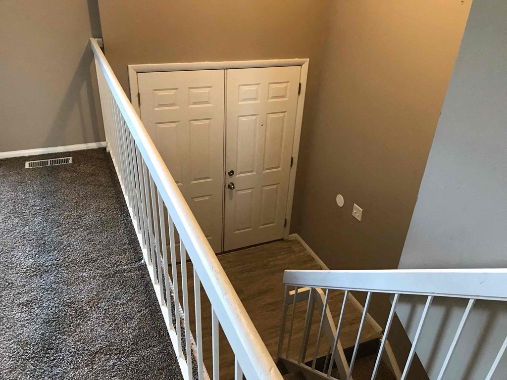 A room with a carpeted floor, a white railing, and a white door.