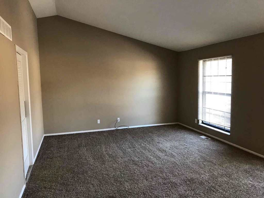 A room with a carpeted floor and a window with blinds.