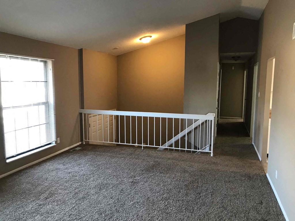 A room with a carpeted floor and a white railing.