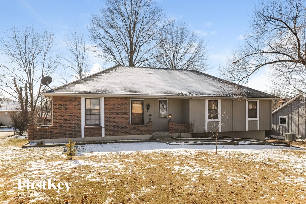 A house with a snow-covered roof and bare trees in the background.