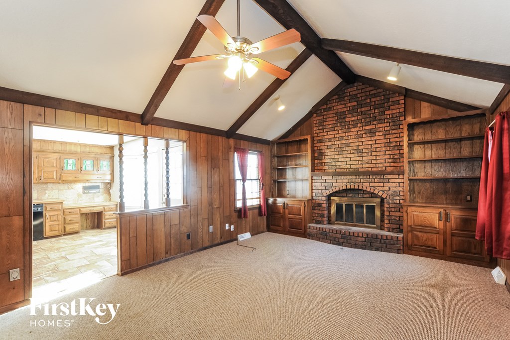 A large, empty room with a fireplace and a ceiling fan.