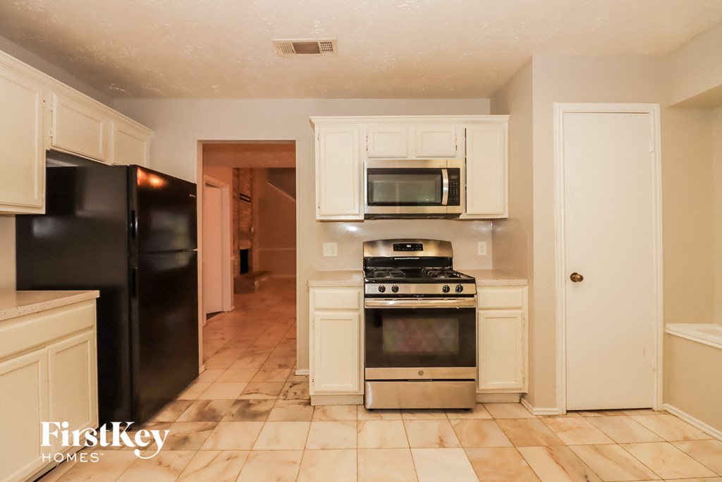 a kitchen with white cabinets and appliances and a black refrigerator