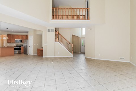 A spacious living room with a kitchen in the background and a staircase leading to the upper floor.