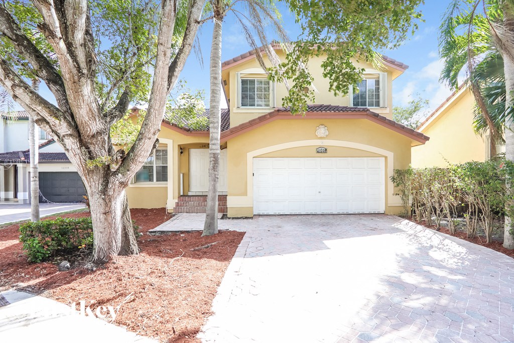 A yellow house with a white garage door and a tree in front.