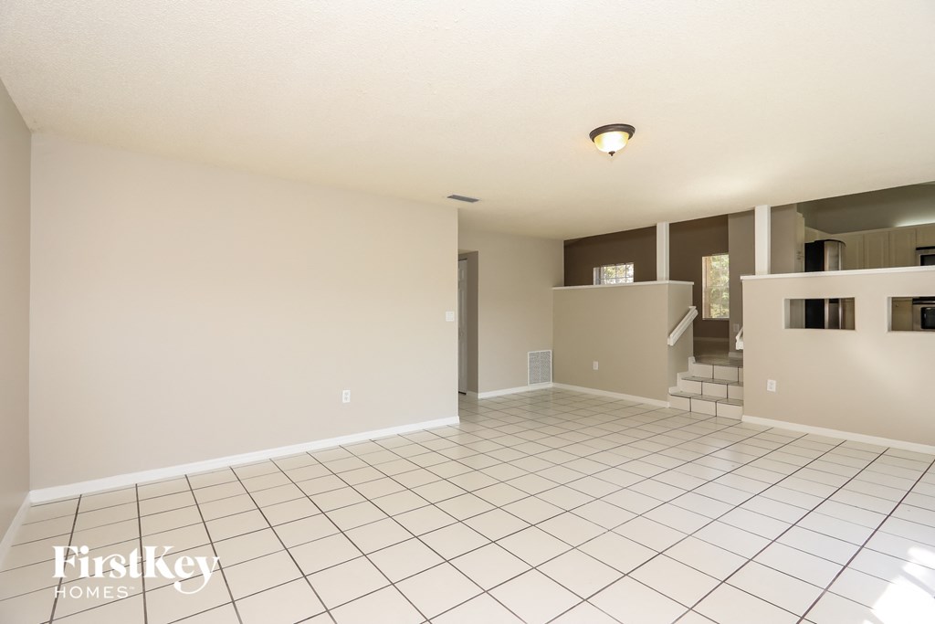 A spacious empty room with tiled flooring and a staircase in the background.
