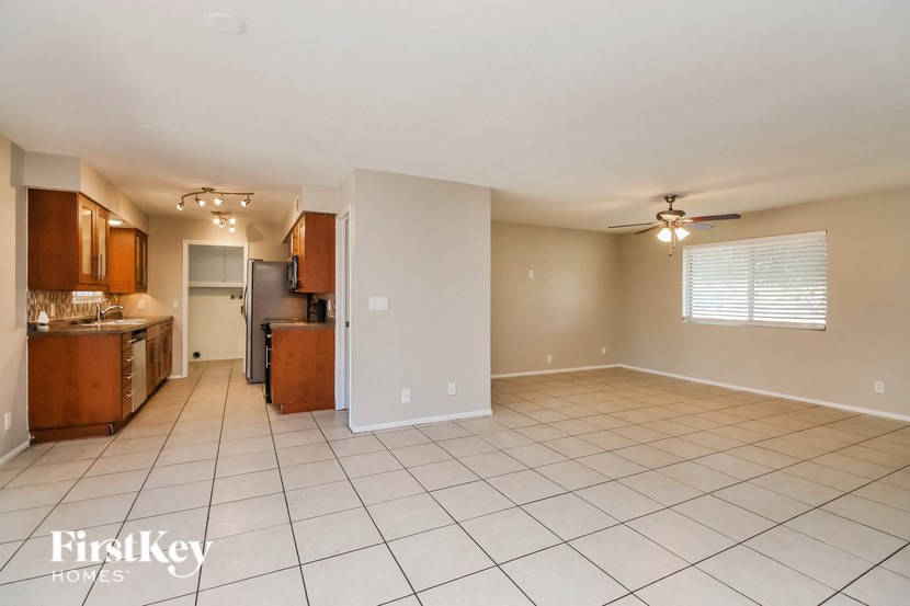 an empty living room with a kitchen and a ceiling fan
