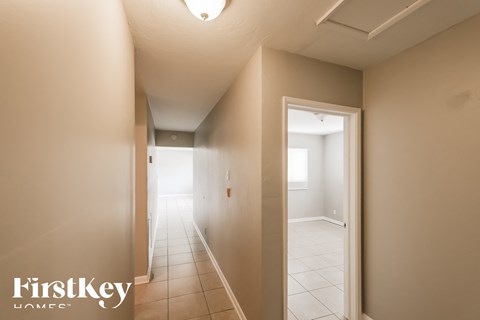 the hallway of a home with a white tile floor and a door to a bedroom
