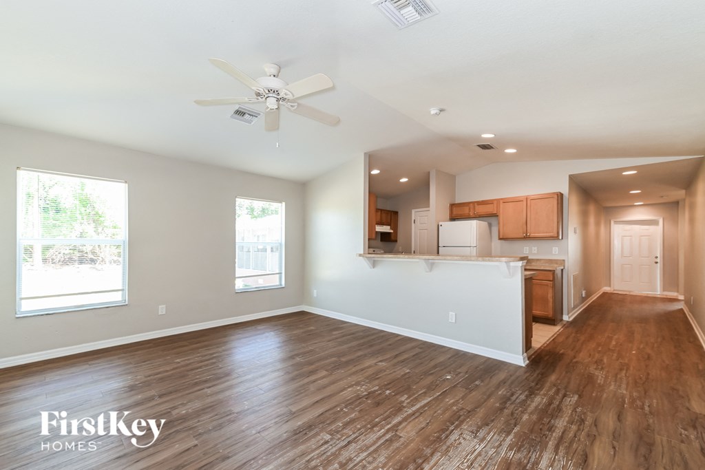 an empty living room with a kitchen and a ceiling fan